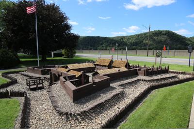 Picture of Fort Augusta Replica with flowing American flag in the background against a pretty blue sky and mountain view in the background.