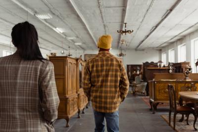 Two adults wearing plaid walk in an antique shop looking at furniture