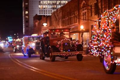 Old fashioned cars with christmas lights attached driving in a parade