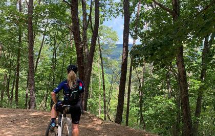 blond female cyclist with gravel bike at forested mountain overlook