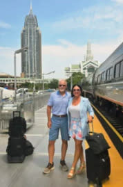 A couple stands on an Amtrak train platform with a skyscraper behind them