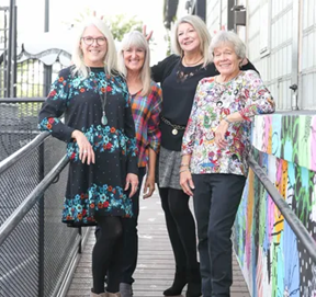 four ladies standing on a walkway leaning on a handrail