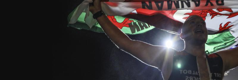 Male Ironman athlete holding a Welsh flag aloft.