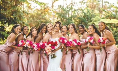 A bride poses with her bridesmaids dressed in pink silk dresses with coordinated hairstyles and tropical pink bouquets in Jamaica