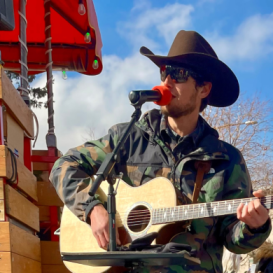 Musician Jeff Goodwin wearing a cowboy hat singing and playing guitar.