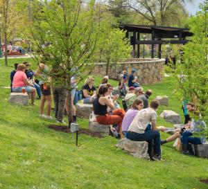 Picture of people sitting on rocks at Hufnagle in Downtown Lewisburg on a sunny spring day with trees in bloom.