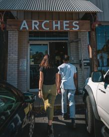 Young woman and man are seen from behind as they walk towards the entrance of Arches Brewing.
