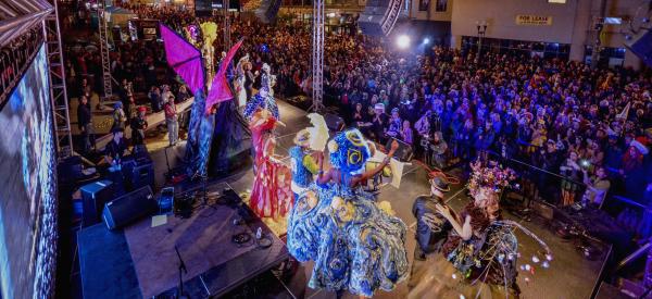 People clothed in elaborate costumes on stage facing large crowd during HighBall Halloween