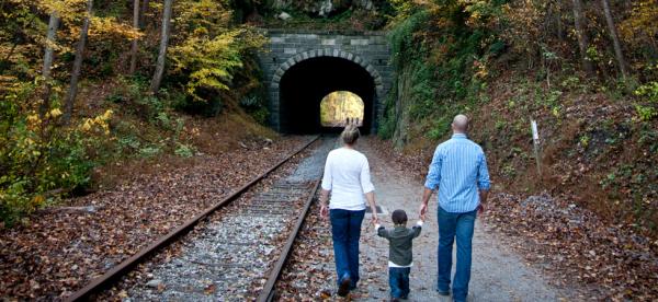 A small child holds hands with their parents as they walk along the rail trail toward Howard Tunnel in fall