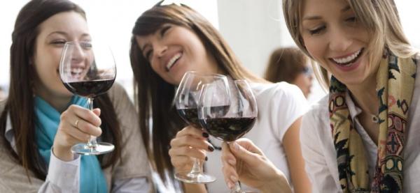 Three young women laugh as they raise their glasses of red wine for a toast