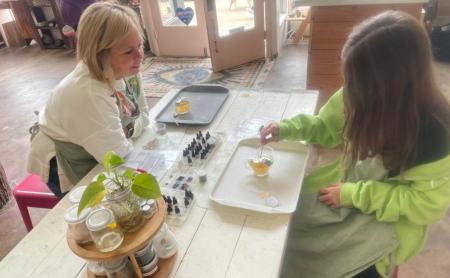 a mom and daughter making candles at a table with botanical ingredients