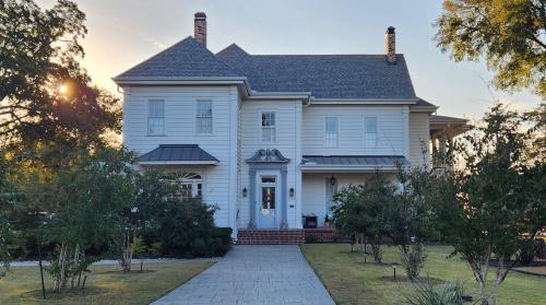 Two story white historic home with sidewalk leading to it and sun going down in the background behind the trees