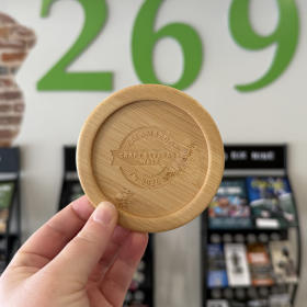 A laser-engraved bamboo coaster features the rounded logo of Kalamazoo Craft Beverage Week