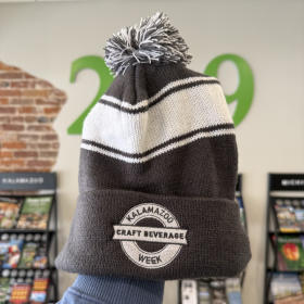 A grey and white hate features the rounded logo of Kalamazoo Craft Beverage Week embroidered on the bottom.