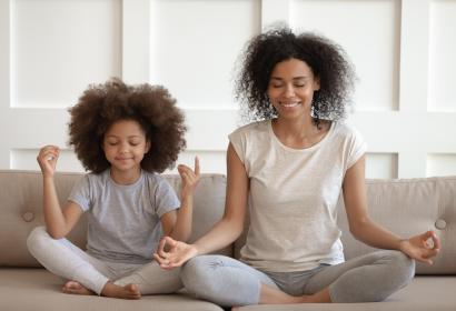 African American mother and daughter meditating on a couch