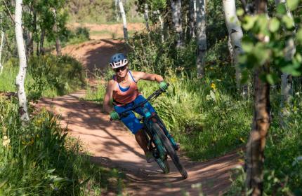 A female mountain biker rides a bermed trail through the woods at Woodward in Park City UT