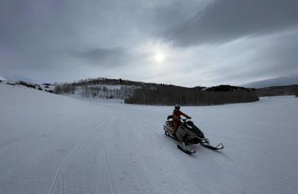 Person riding a snowmobile in a vast landscape of snow.