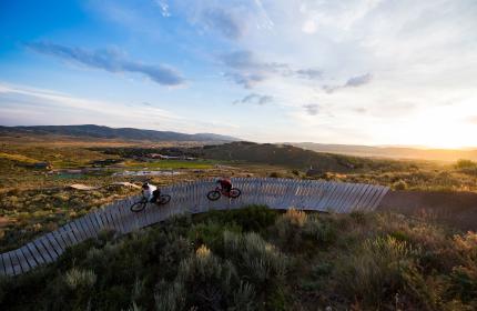 Two mountain bikers riding a rainbow rail in bike park