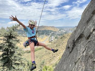A young teen hangs from a top rope while jumping back and belaying down while rock climbing in Clear Creek Canyon Park.