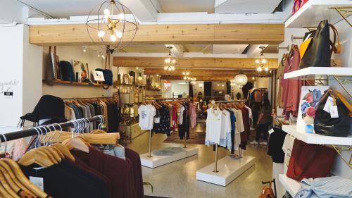 Remedy Road's store interior showcases exposed wooden beams, rustic yet modern light fixtures, and displays of clothing, handbags, and accessories.