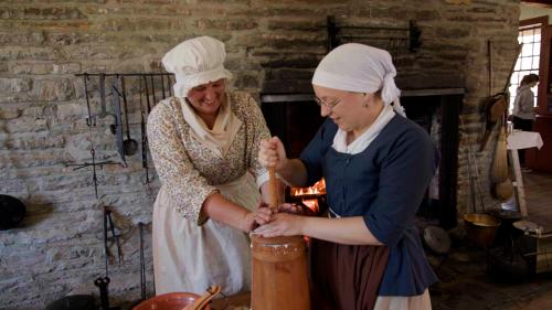 Two women in 18th century garb churning butter