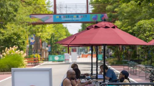 A view down one of the lanes of Ridge Hill Shopping Center. People are seated at outdoor dining tables.