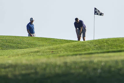 One golfer watching another attempt a putt on the green.
