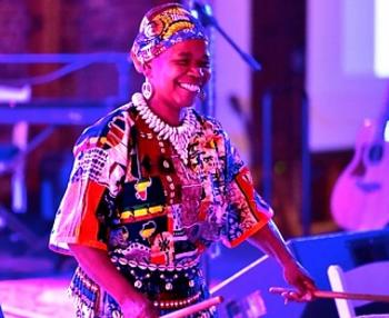 A black woman in African dress drumming