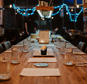 Image shows the table ready for guests at Feasted, with chefs working and pretty lights in the background