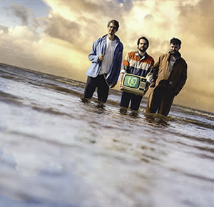 Three men stand knee deep in sea water