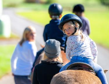 Young white girl looking over her shoulder on a horse being lead by an instructor