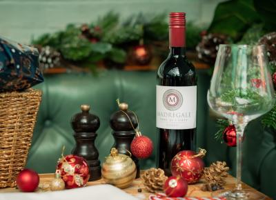 A bottle of red wine on a restaurant table with an empty wine glass beside it. There are also #Christmas baubles, a wooden condiment set & a wicker basket in the image - Fellows House #Cambridge