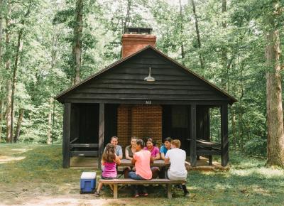 Group of people at a picnic table in front of a cabin in the forest
