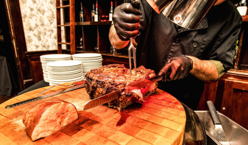 gloved hands carving prime rib on a chopping block