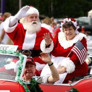 Mr and Mrs Santa Claus waving to a crowd from a vehicle in a parade