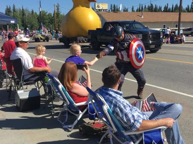 Man dressed in Captain America costume shaking hands with a young parade spectator