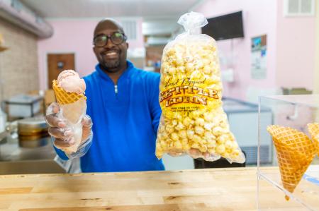 Man reaching over wooden counter holding an ice cream cone and bag of popcorn