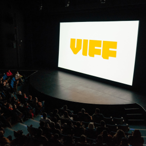 [ID: a photo of a movie theater screen, it's a white background with bold yellow text that reads: VIFF. Vancouver International Film Festival 2024 occurs from September 26, 2024 - October 6, 2024.]