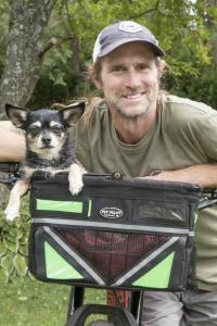 person smiles on a bike with a small dog in the bike basket