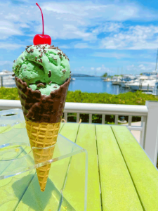 Ice cream cone in a holder on a table with a view of blue sky, blue water, and boats in a marina