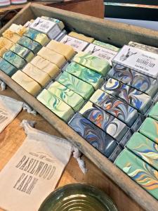 Colorful soaps arranged on wooden shelf next to basilwood farm soap pouches