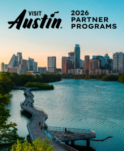 Hike and Bike Trail boardwalk along Lady Bird Lake, looking towards downtown with the words "Visit Austin 2026 Partner Programs" at the top and "Live Music Capital of the World" at the bottom.