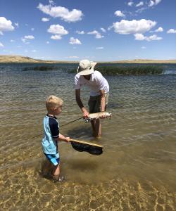 father and son holding trout in lake