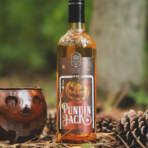 A bottle of Punkin Jack wine from Harvest Ridge Winery is shown sitting amongst pinecones, a copper pumpkin mug, and some fall leaves.