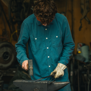 Young boy crafting a sword on an anvil with a metal hammer