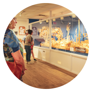 visitors look through glass at a large carved wood scene