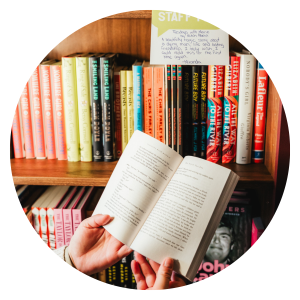 Image of hands holding a book open in front of a shelf full of local author books