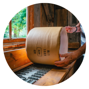 Image of someone rolling a replical wheel of cheese on a historic press they would have used to label the cheese batch.