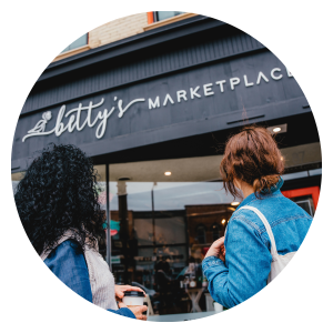 Circular image of two people standing out front of Betty's Marketplace storefront.