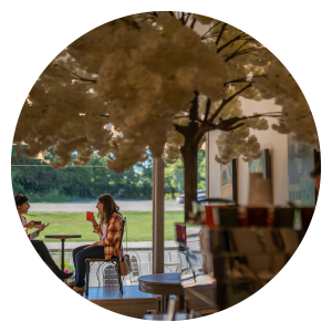 Circular image of two people enjoying cafe drinks at Early Bird Roastery & Cafe